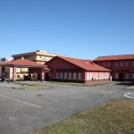 赤茶色の屋根と木製外壁の介護施設の建物外観。駐車場が見える。