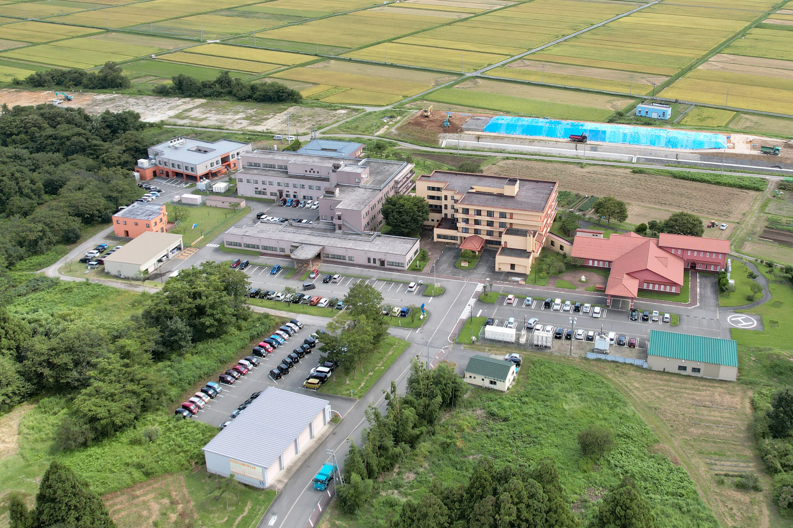 複数の建物と駐車場を備えた介護施設の全体空撮写真。農地に囲まれた立地。